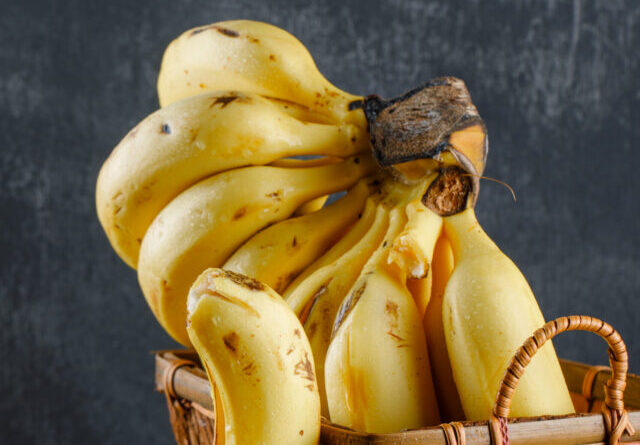 Bananas in a basket on wooden and plaster background. side view.